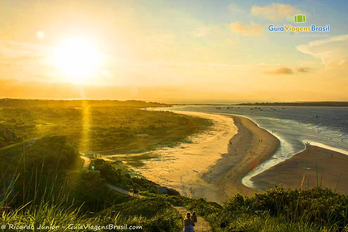 Imagem de turistas descendo o caminho do Farol e um lindo pôr do sol acontecendo, na Ilha do Mel, Paraná, Brasil.