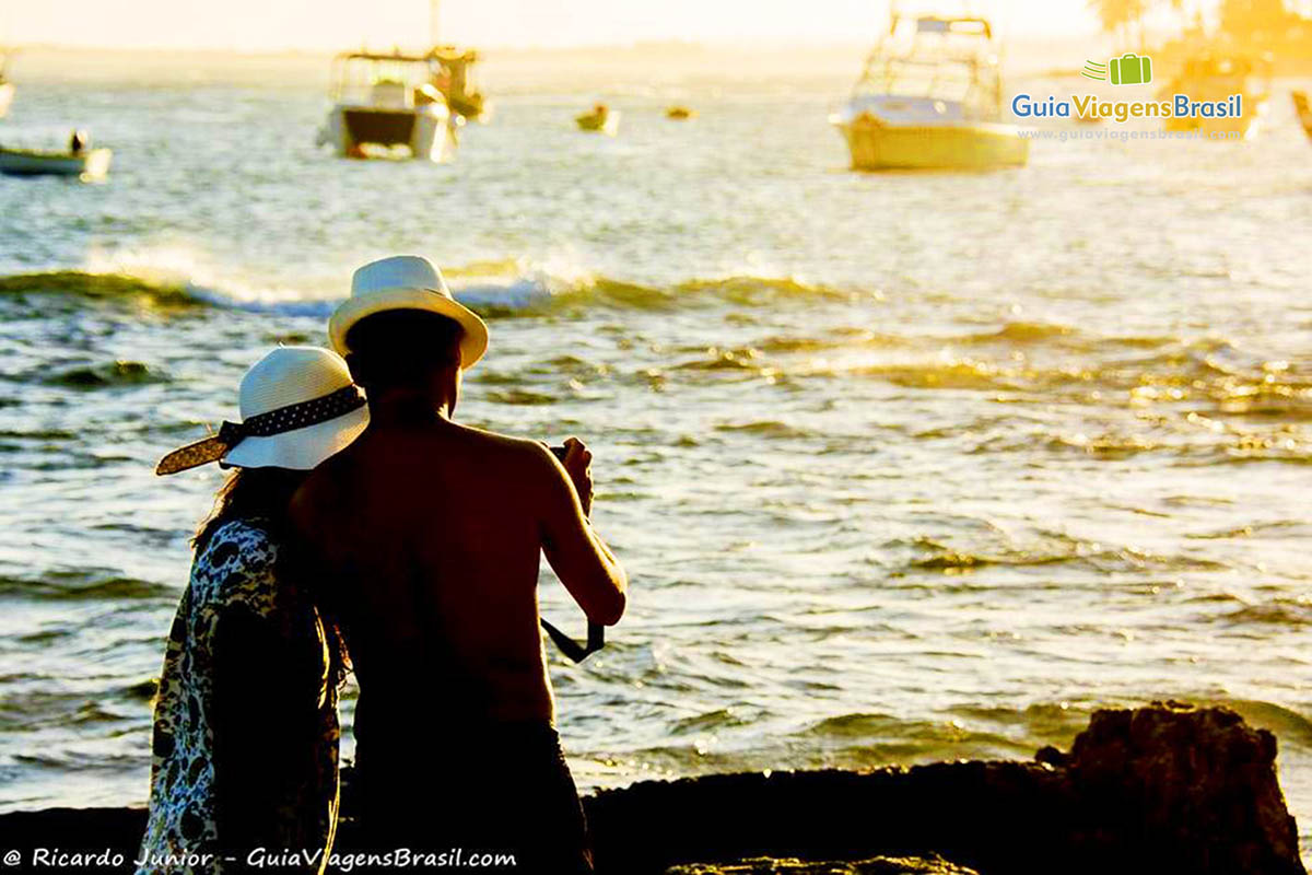 Imagem de casal admirando o pôr do sol. 