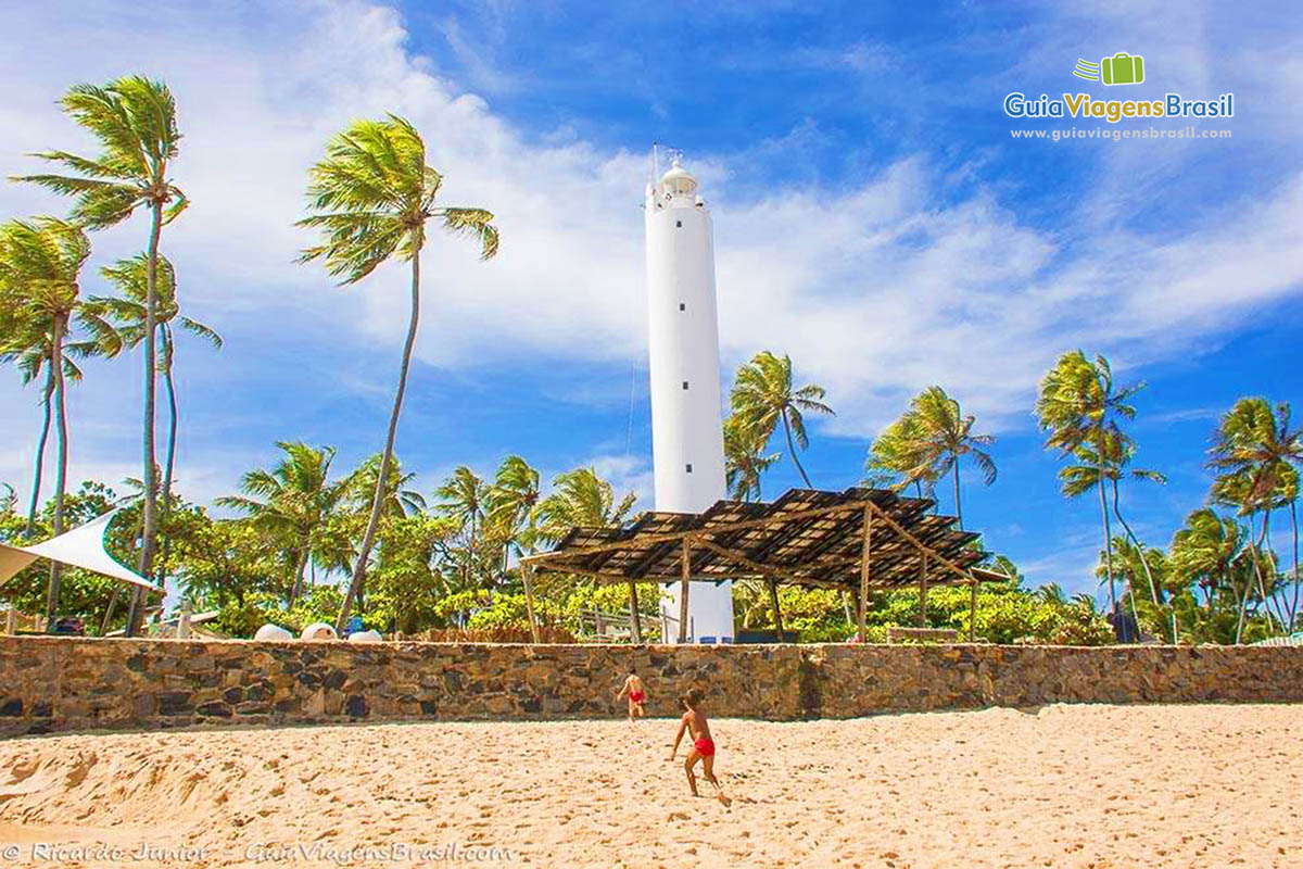 Imagem da areia da praia a ao fundo o farol com os coqueiros, na Praia do Forte, Bahia.