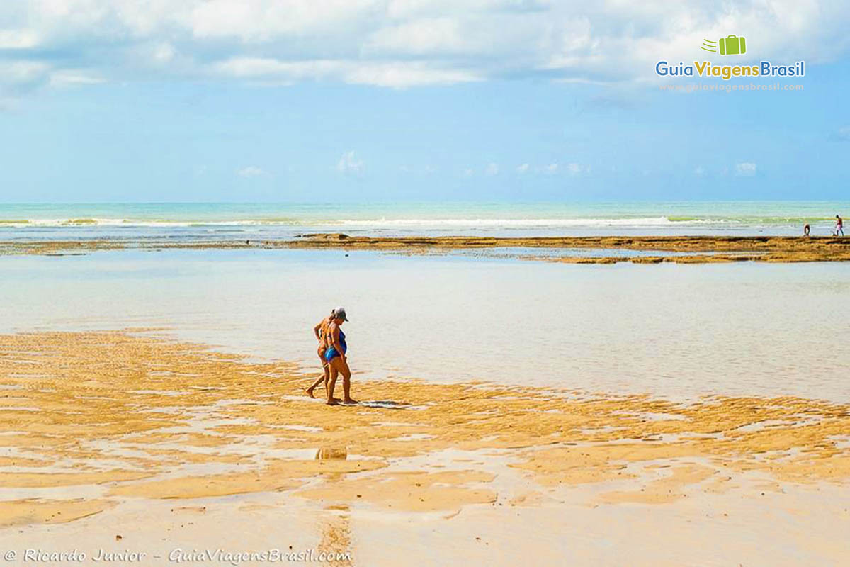 Imagem de pessoas caminhando nas piscinas naturais da Praia do Mucugê. 