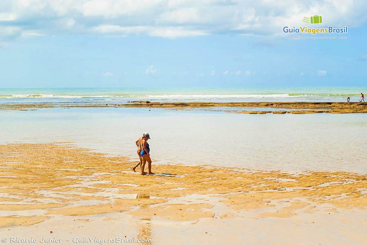 Imagem de pessoas caminhando nas piscinas naturais da Praia do Mucugê. 