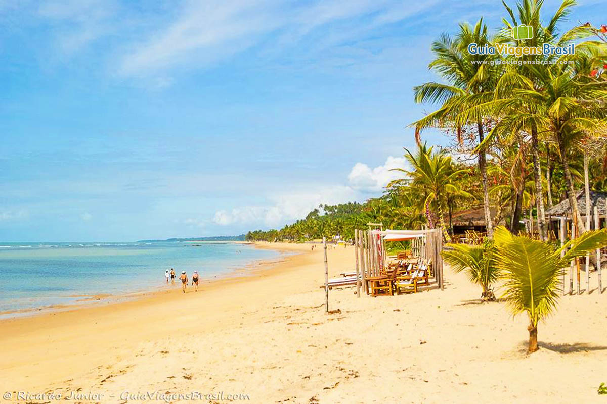 Imagem de pessoas caminhando em belo dia na Praia Mucugê.