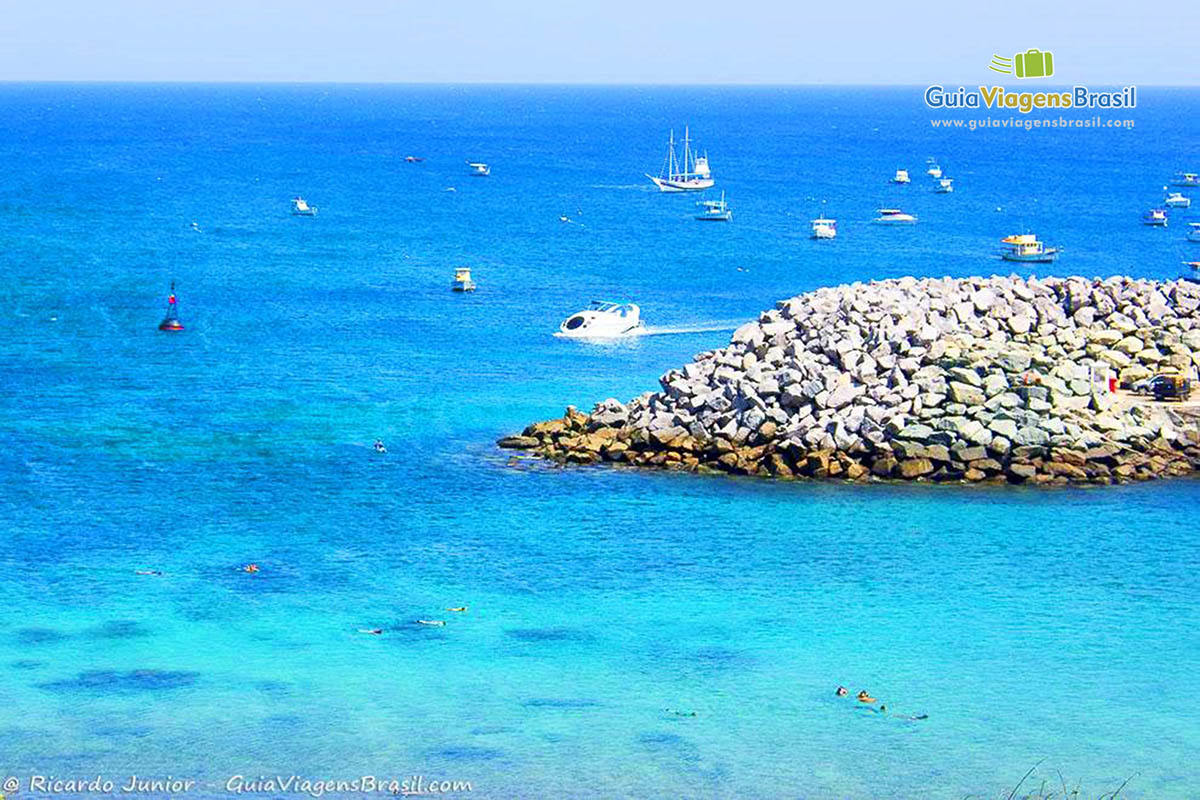 Imagem de barcos mais ao fundo do mar e turistas mergulhando na praia de Porto Santo Antônio, em Fernando de Noronha, Pernambuco, Brasil.