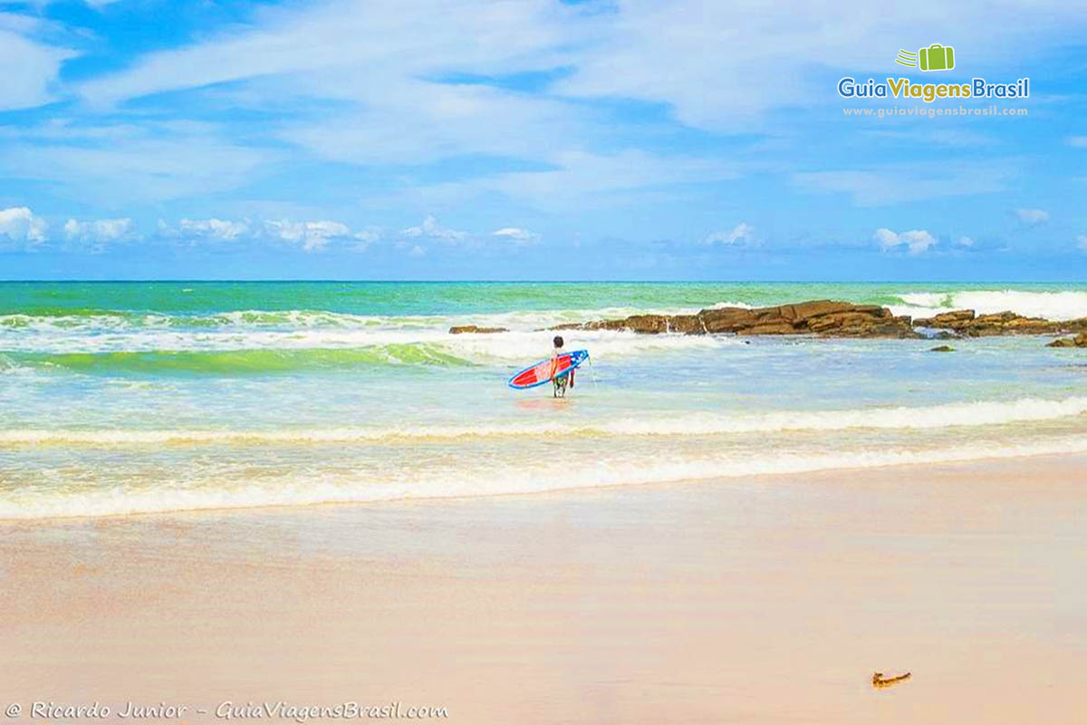 Imagem de surfista entrando nas águas da praia.