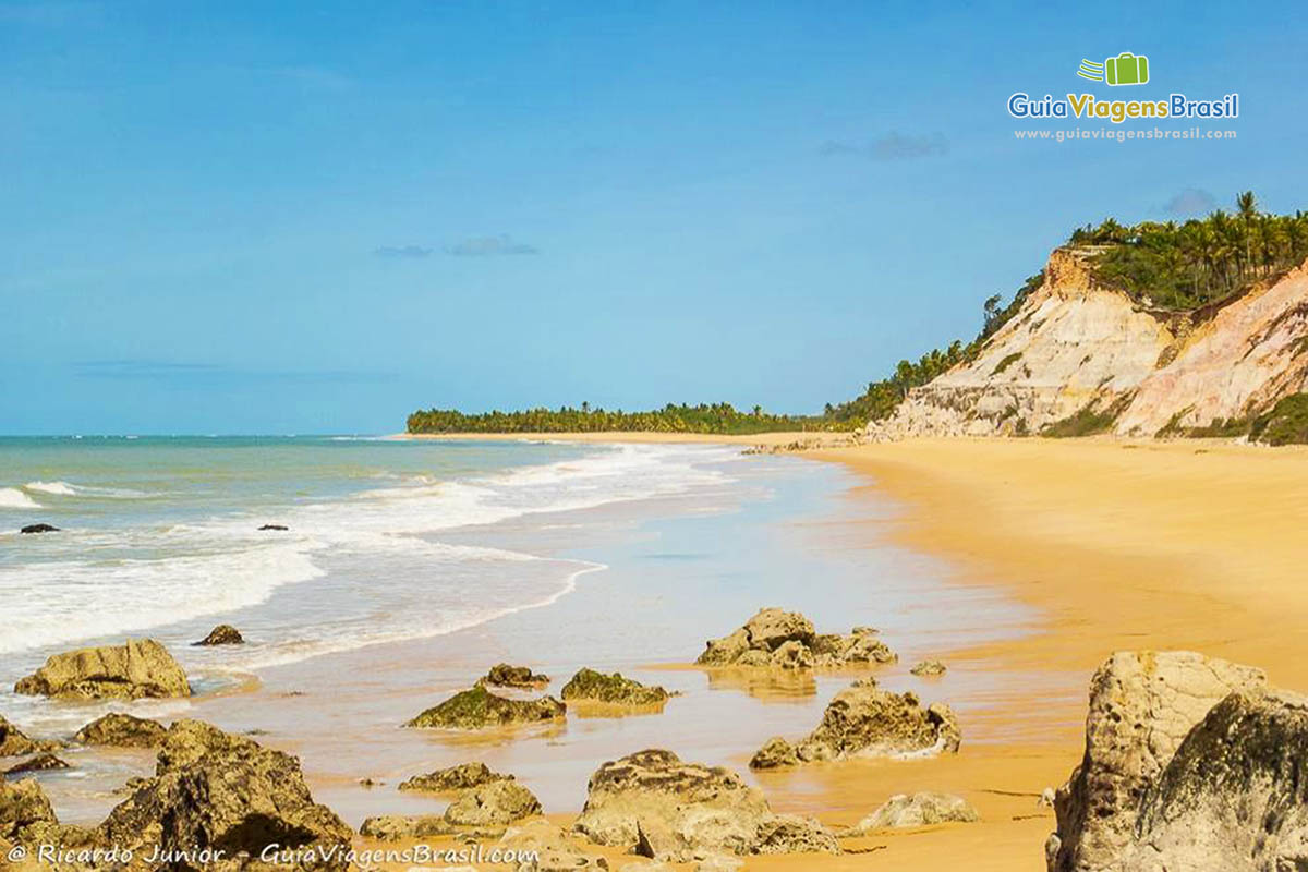 Imagem das águas batendo nas pedras no canto da praia.