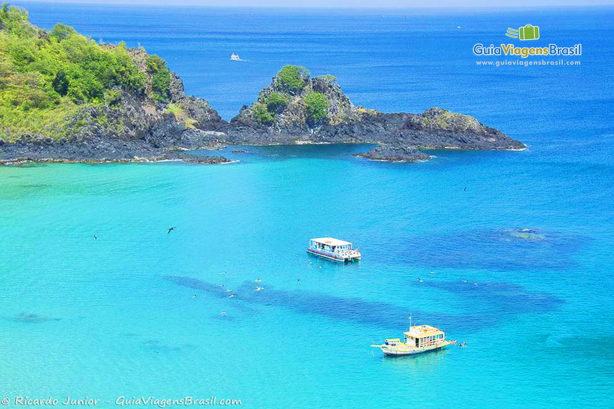 Imagem do alto, de dois barcos parados em alto mar aguardando turistas que estão mergulhando e pássaros voando, na Praia do Sancho, em Fernando de Noronha, Pernambuco, Brasil.