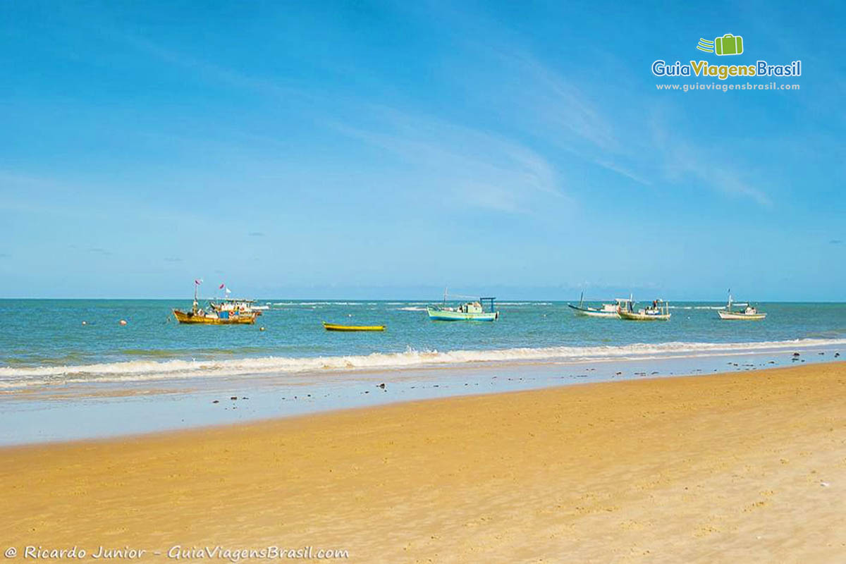 Imagem de barcos de pescadores na águas azuis da praia.