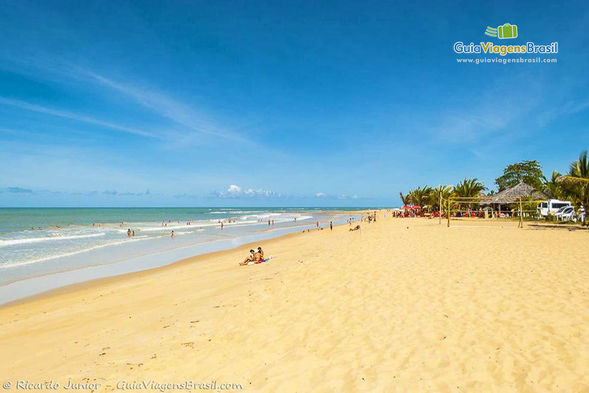 Imagem de turistas no mar e outros na areia da Praia dos Nativos.