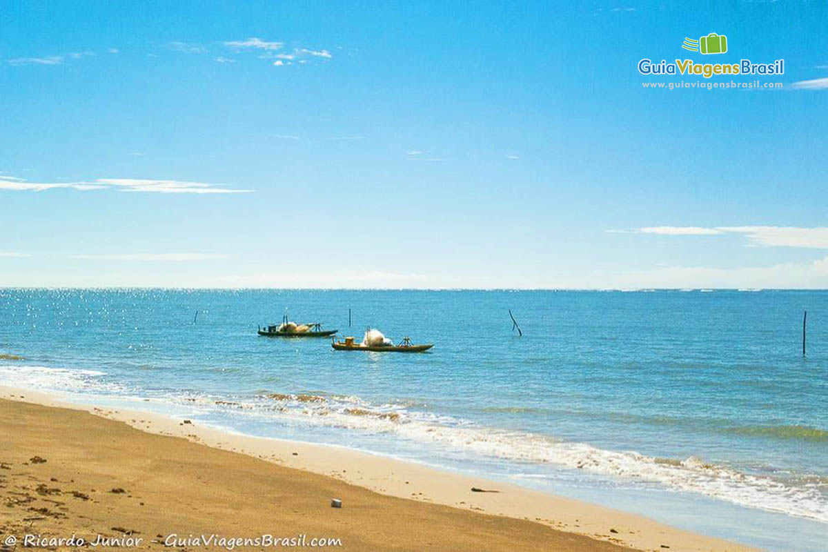 Imagem da luz do sol refletindo nas águas do mar e tem dois barcos de pescadores parado.