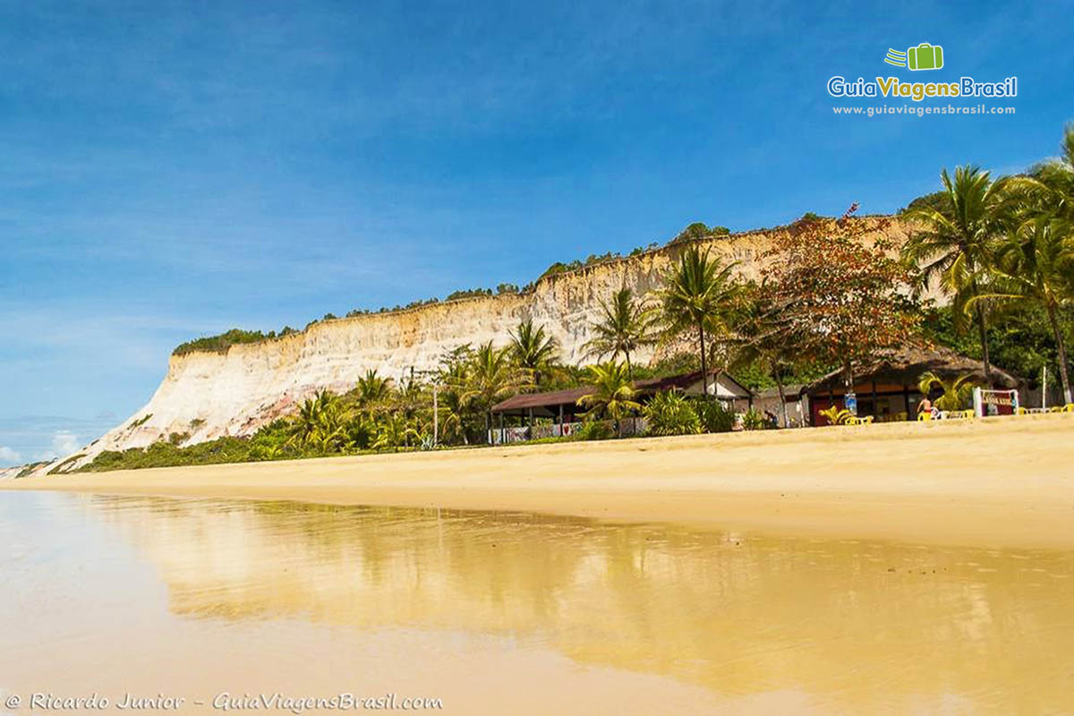 Imagem das águas transparentes da praia e quiosque ao fundo.