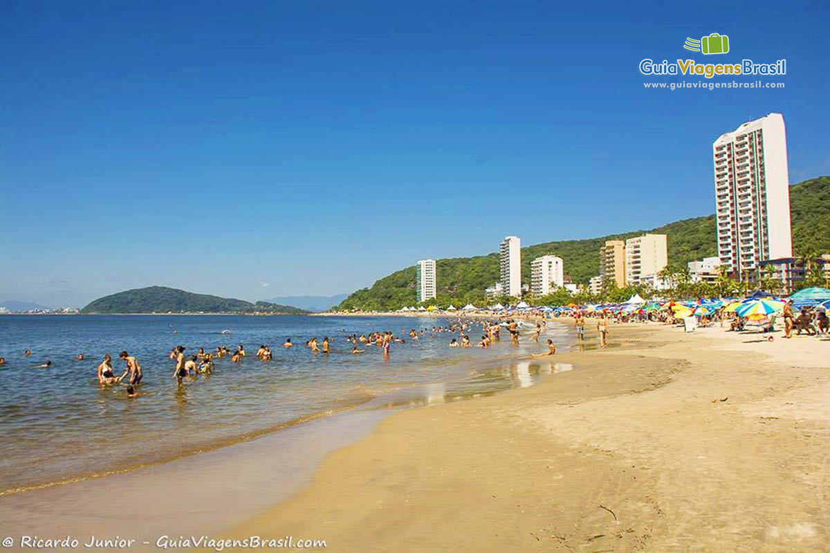 Imagem de turistas nas águas calmas e alguns prédios que possui na orla da Praia Mansa, em Caiobá, Santa Catarina, Brasil.