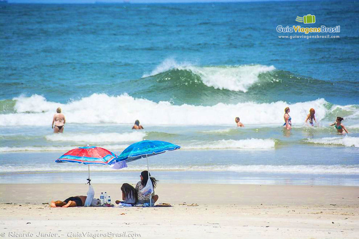 Imagem de família embaixo do guarda-sol aproveitando a bela visão da Praia Mar de Fora das Encantadas, na Ilha do Mel, Paraná, Brasil.