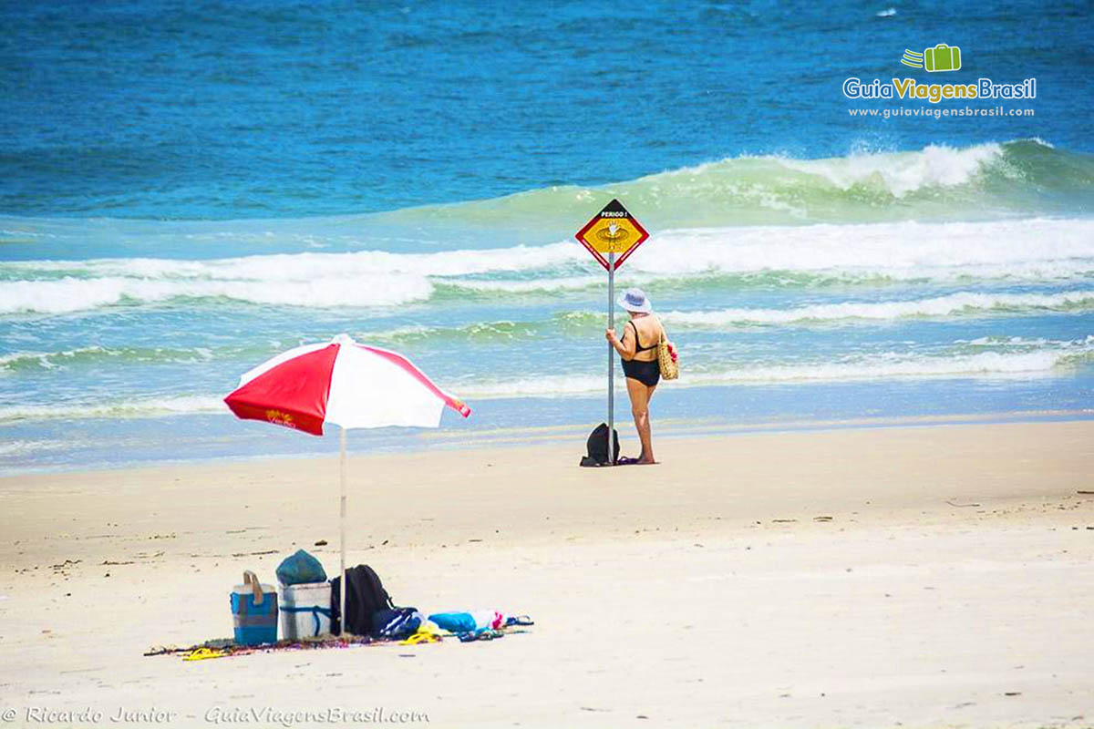 Imagem de uma turista parada na beira do mar admirando a Praia Mar de Fora das Encantadas, na Ilha do Mel, Paraná, Brasil.