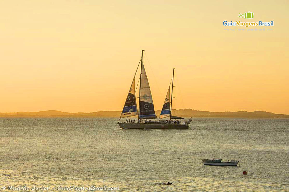 Imagem do barco a velas no mar e ao fundo o pôr do sol encantador.