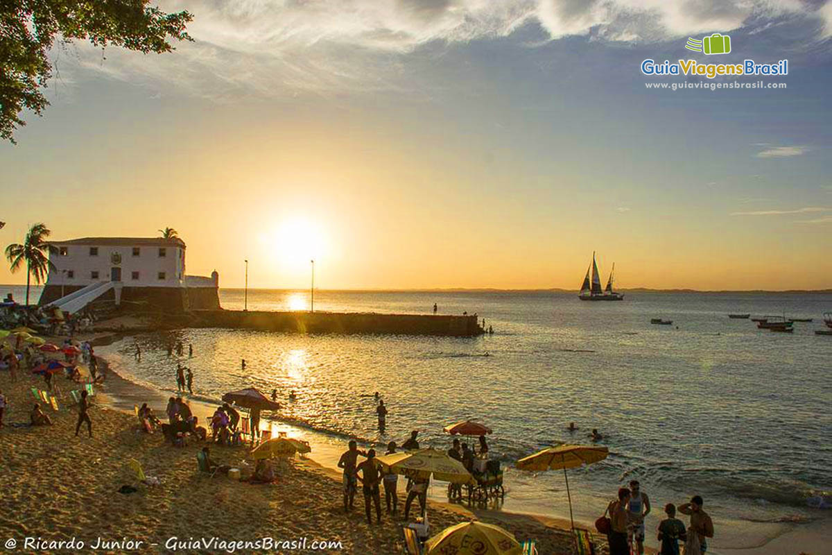 Imagem de turistas aproveitando até último minuto do sol na Praia Porto da Barra.