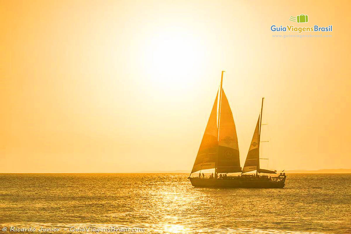 Imagem do barco a velas no mar e sol com uma cor alaranjado.