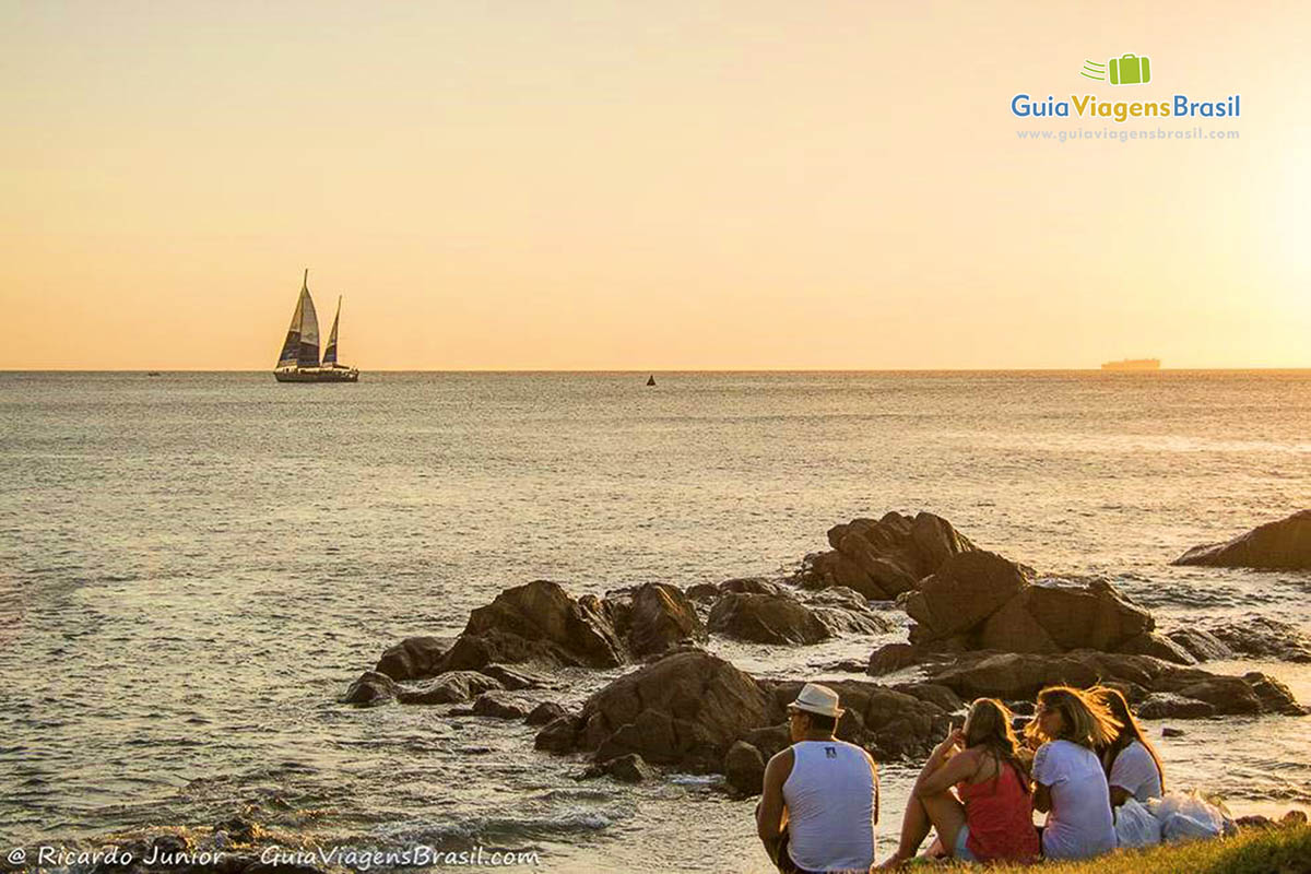 Imagem de turistas sentados e admirando o pôr do sol.