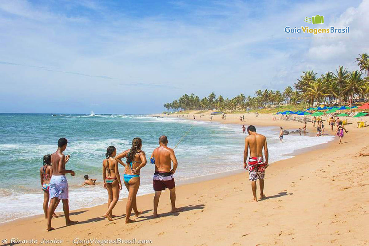 Imagem de turistas caminhando na areia da praia.