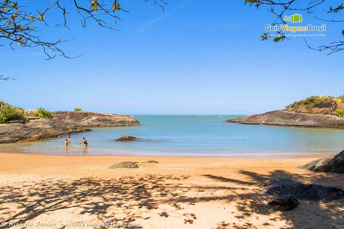 Imagem de três pessoas nas águas da Praia Vermelha.