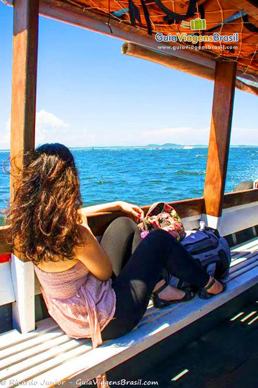 Imagem de turista sentada no barco admirando a paisagem da travessia para Ilha do Mel, Paraná, Brasil.