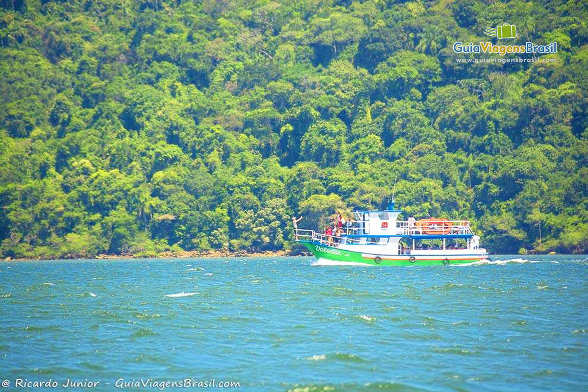 Imagem do barco de travessia em alto mar e ao fundo vegetação da Ilha do Mel, Paraná, Brasil.