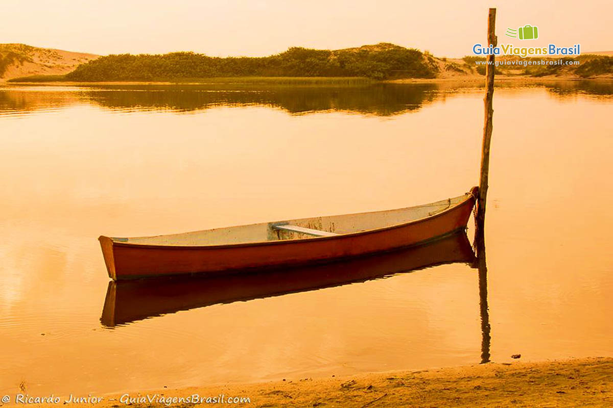 Imagem de um único barco na beira da praia com uma luz do céu alaranjado do entardecer.