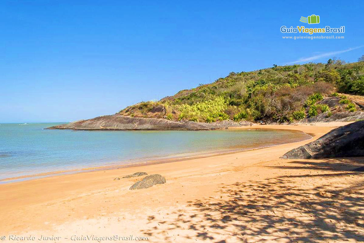 Imagem do canto da praia, com um pouco de vegetação nas pedras.