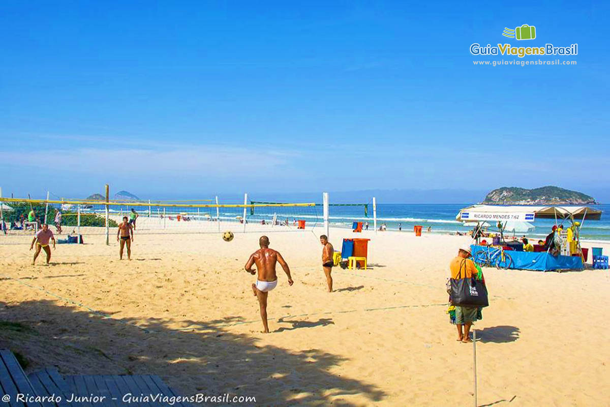 Imagem de amigos jogando futevôlei na praia.