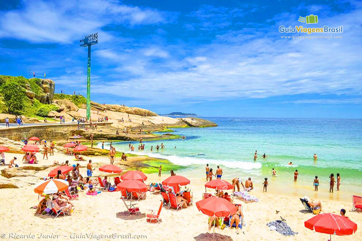 Imagem de uma praia cheia de visitantes em um belo dia de sol.