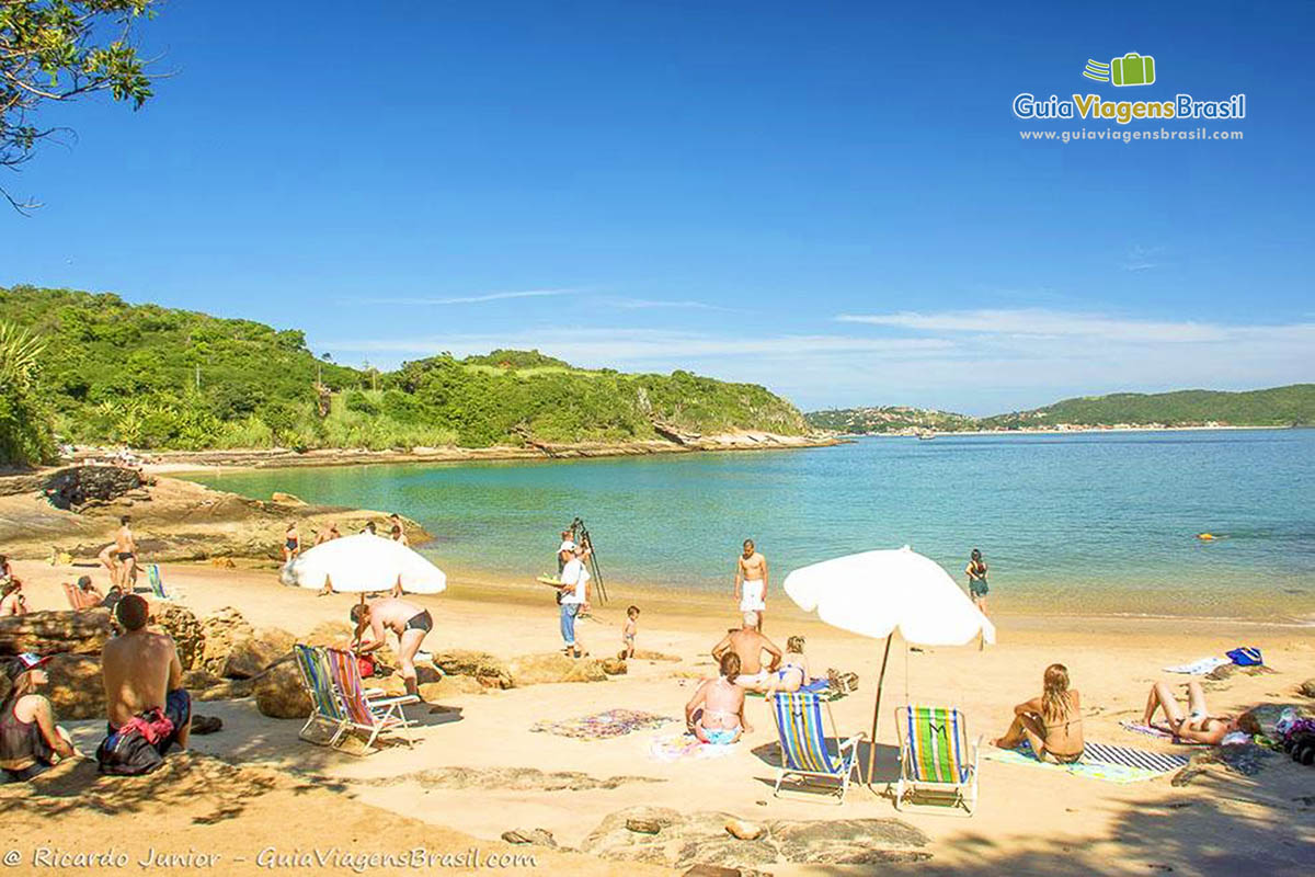 Imagem de dois guarda sol na areia e visitantes espalhados pela praia.