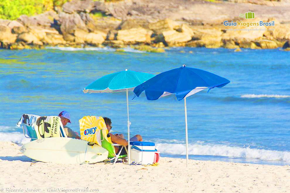 Imagem de dois amigos embaixo de seus guarda sol na linda Praia Cambury.