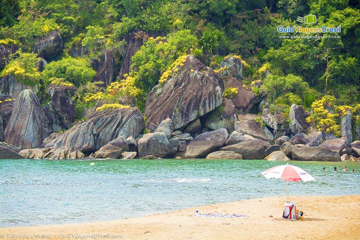 Imagem de guarda sol nas areias da praia e ao fundo umas pessoas nas águas da praia.