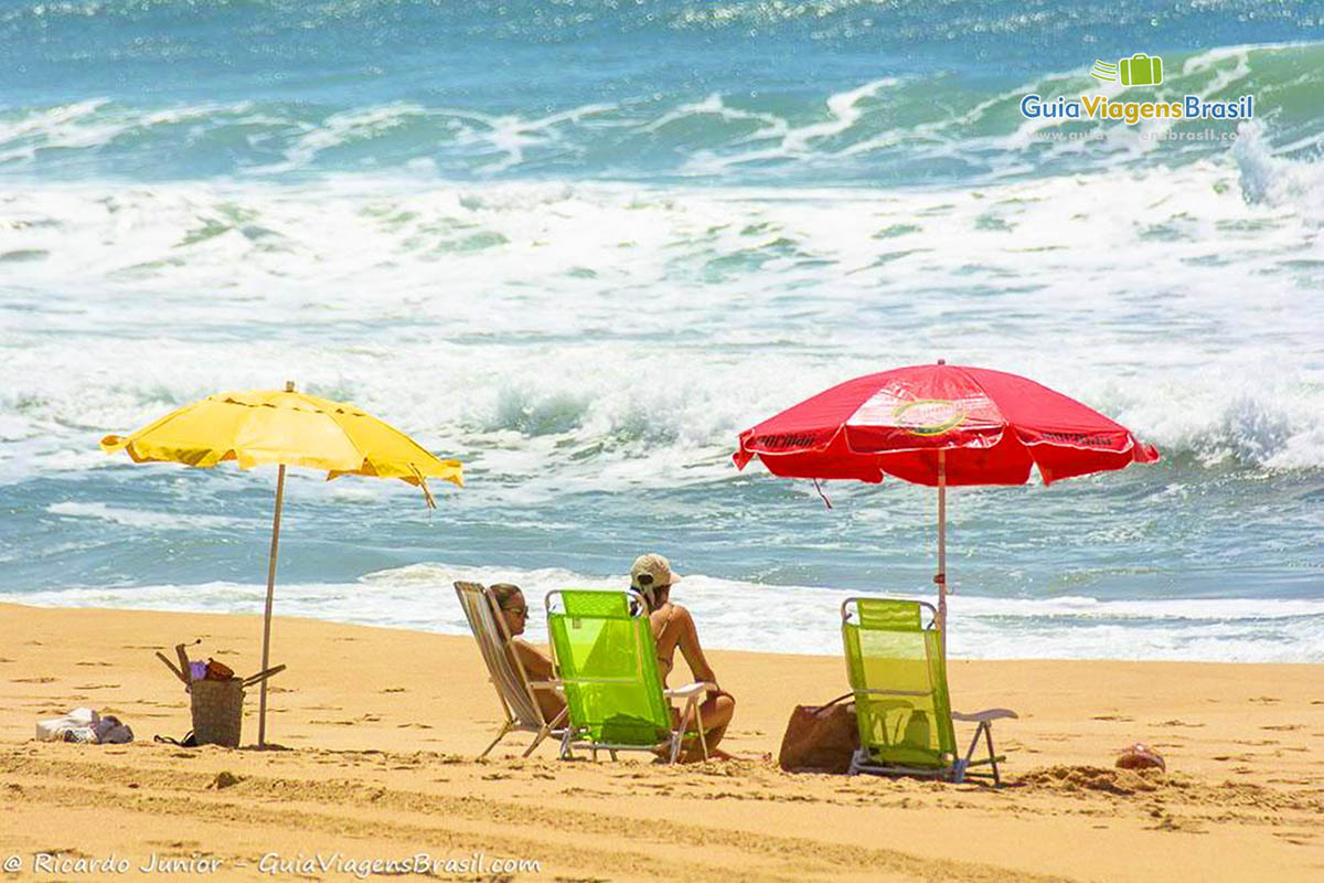 Imagem de turistas com guarda sol coloridos na Praia Silveira.