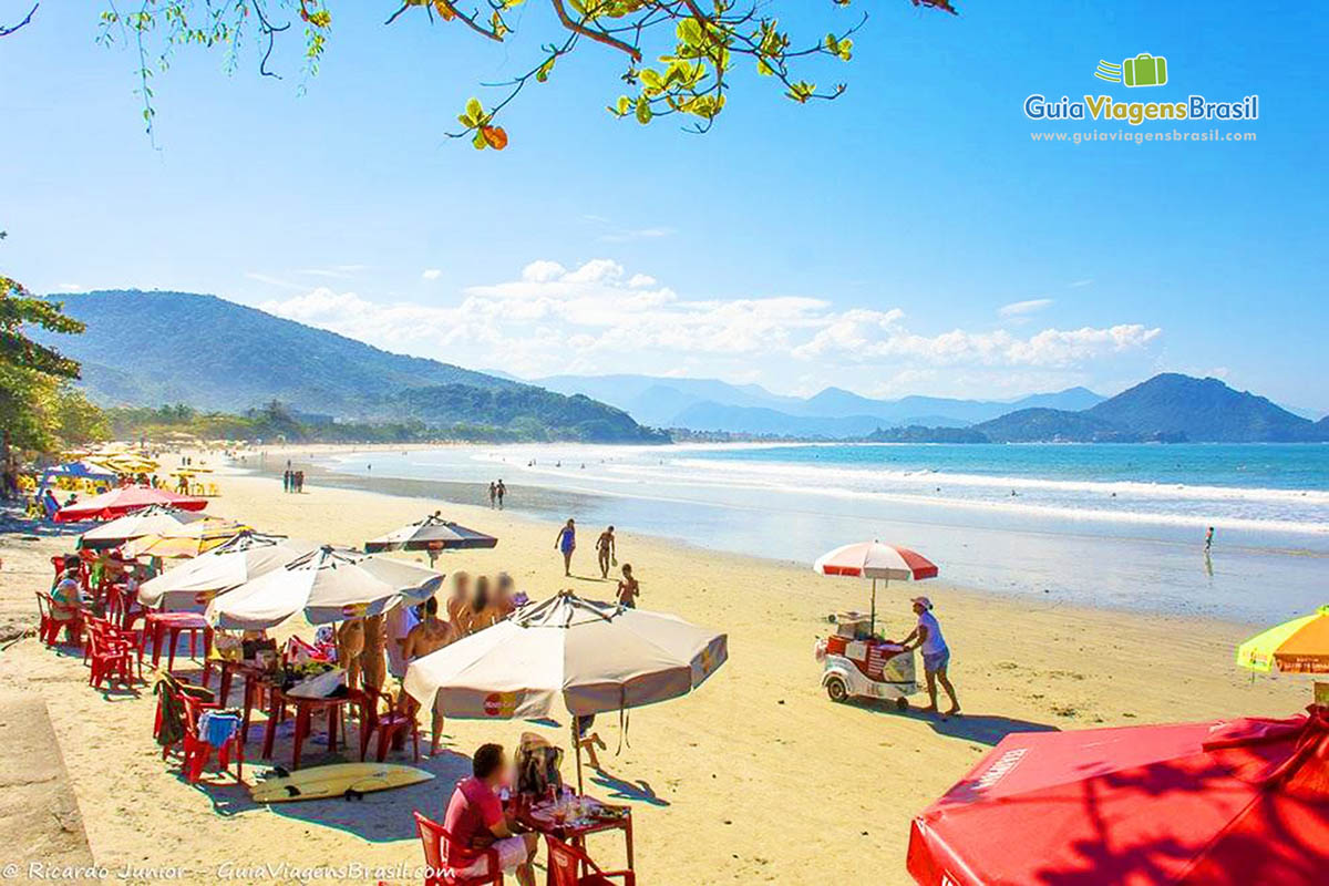 Imagem de turistas em baixo de seus guarda sol nas areias da Praia das Toninhas.