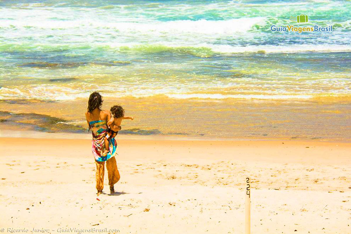 Imagem de uma moça com filho no colo olhando para o mar.
