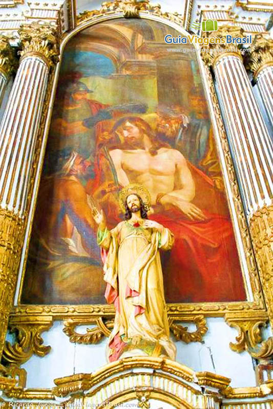 Imagem de um santo e pintura na parede atrás do mesmo santo.