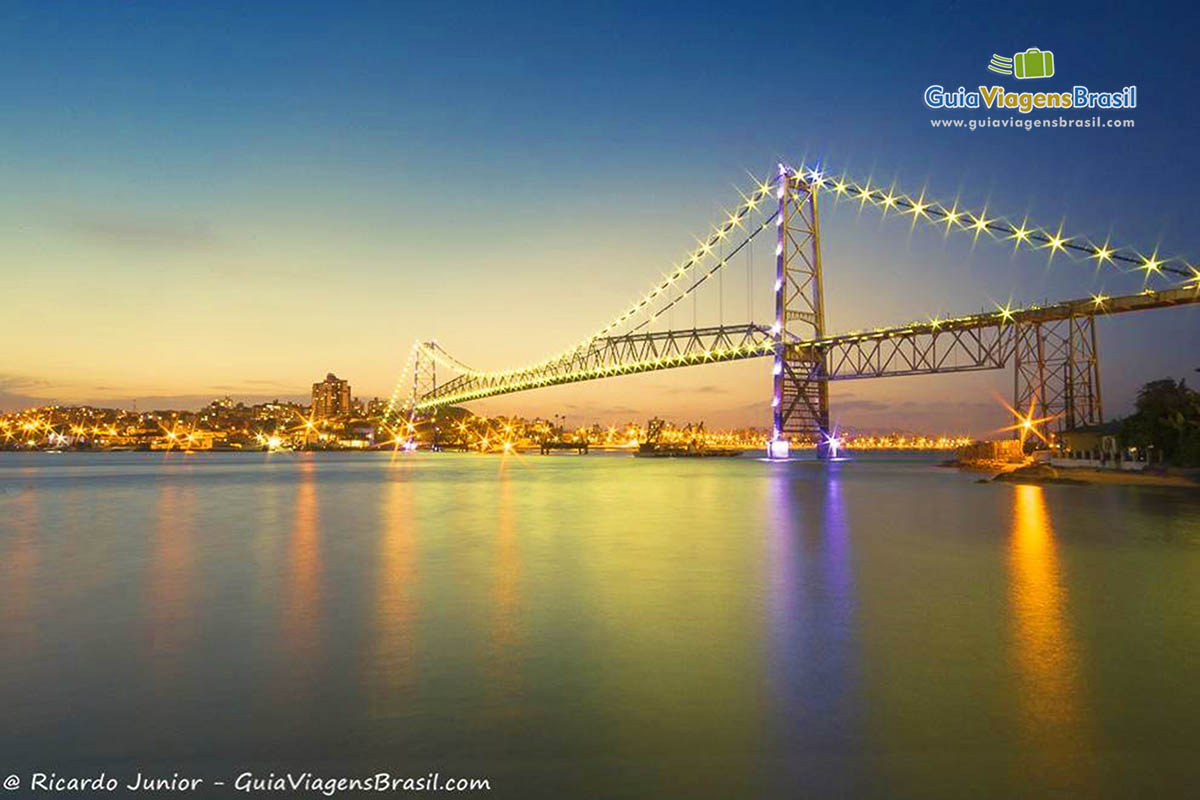 Imagem do anoitecer na ponte toda iluminada.