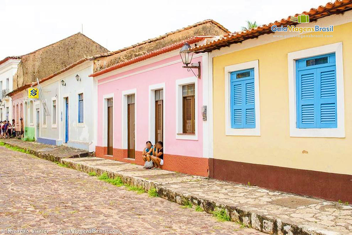 Imagem de moradas sentadas na porta de sua casa, vendo movimento dos turistas na cidade.