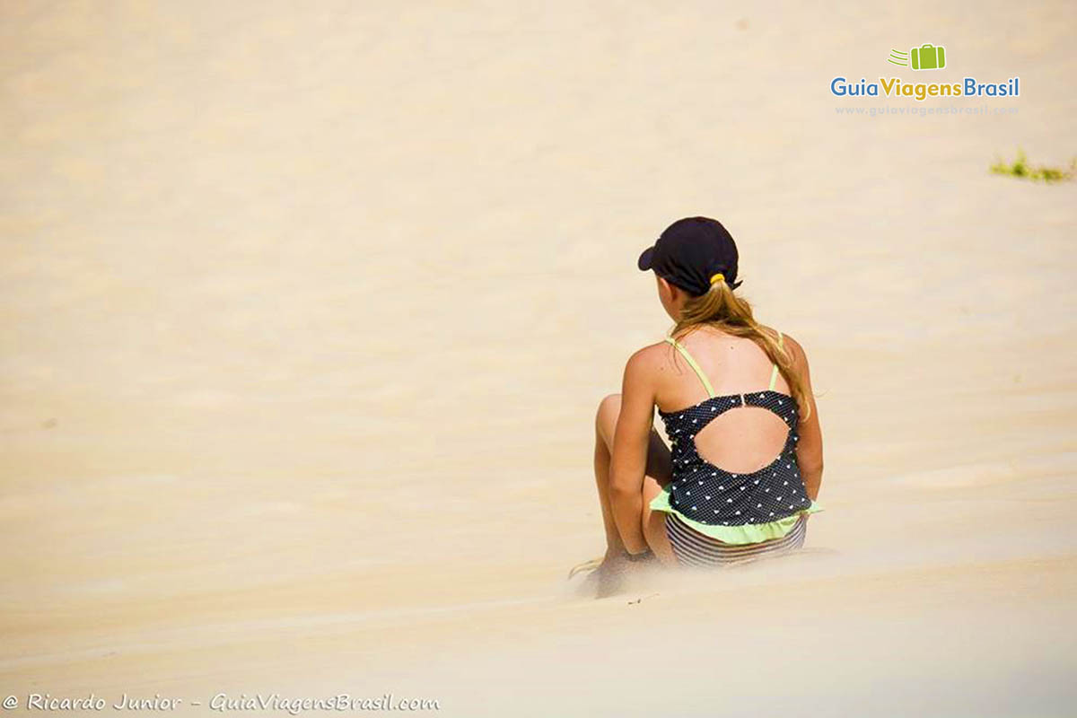 Imagem de uma menina descendo as dunas sentada na prancha.