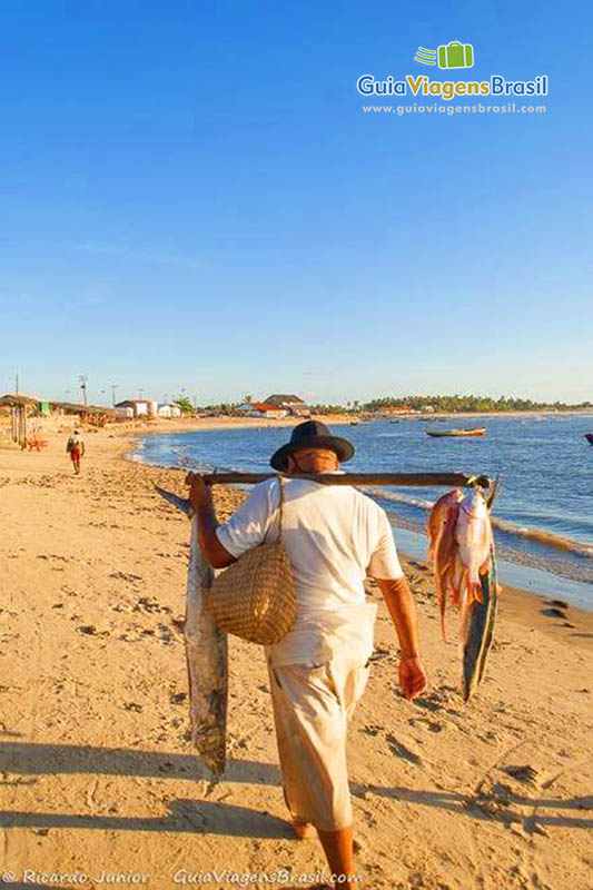 Imagem de pescador carregando peixes pendurados em uma vara.
