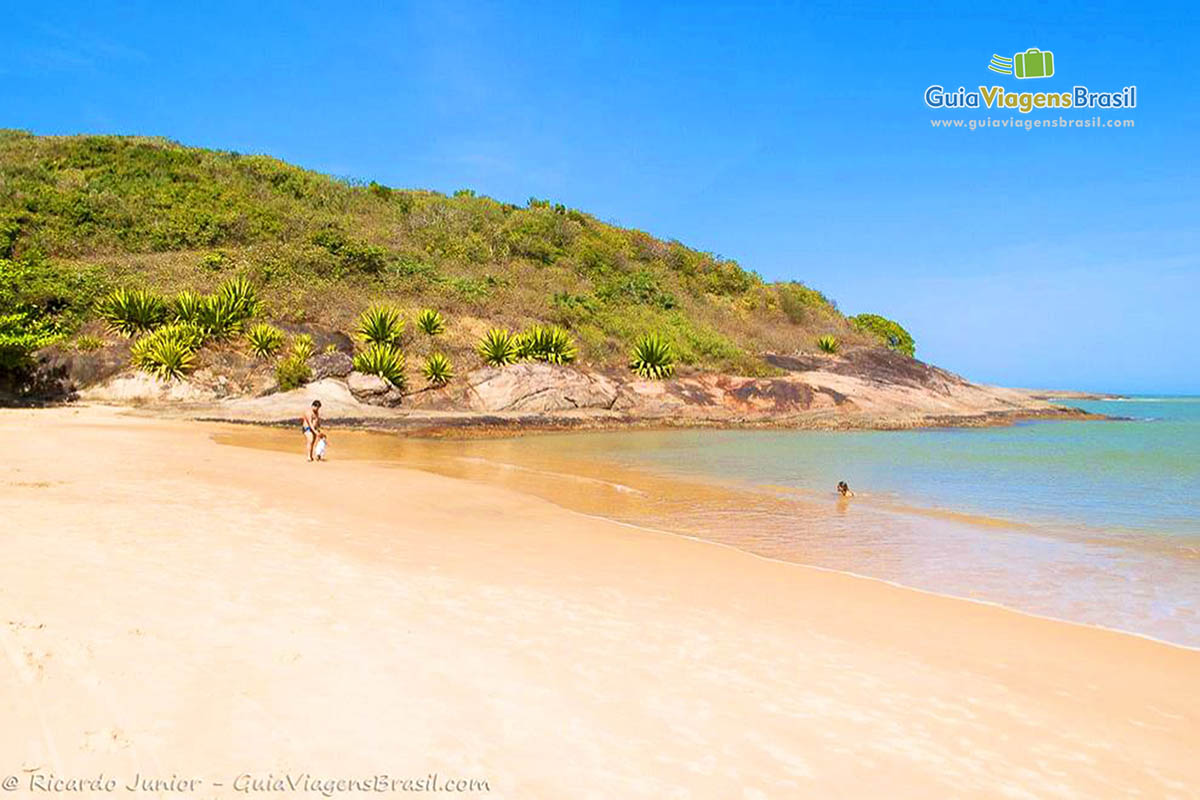 Imagem de pai e criança na beira da praia e a criança apontando para uma pessoa na água.