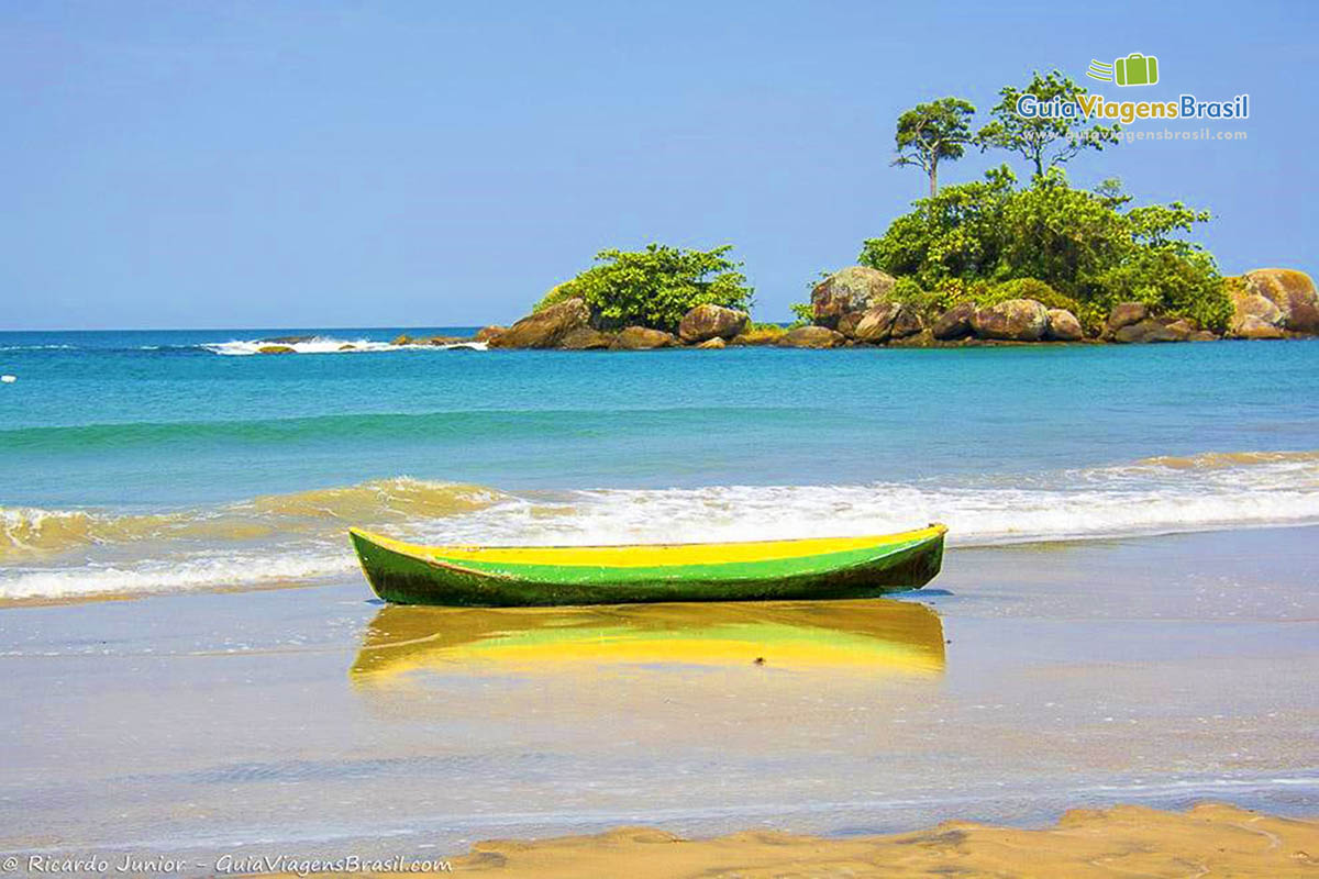 Imagem de um belo barco de pescador e ao fundo as águas azuis encantadoras da lindíssima praia.