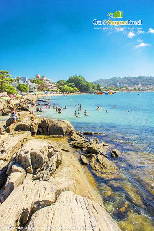 Imagem das pedra e ao fundo pessoas no mar azul da Praia Lagoa Azul.