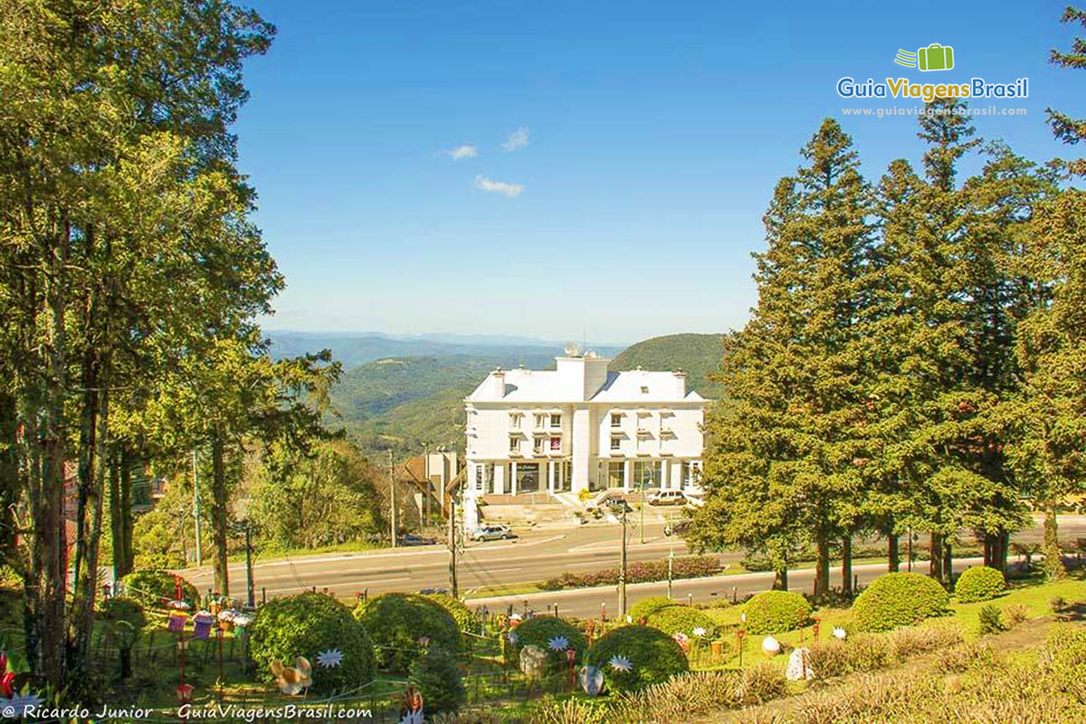 Imagem de um lindo jardim e ao fundo uma loja grande e morro verde maravilhoso.