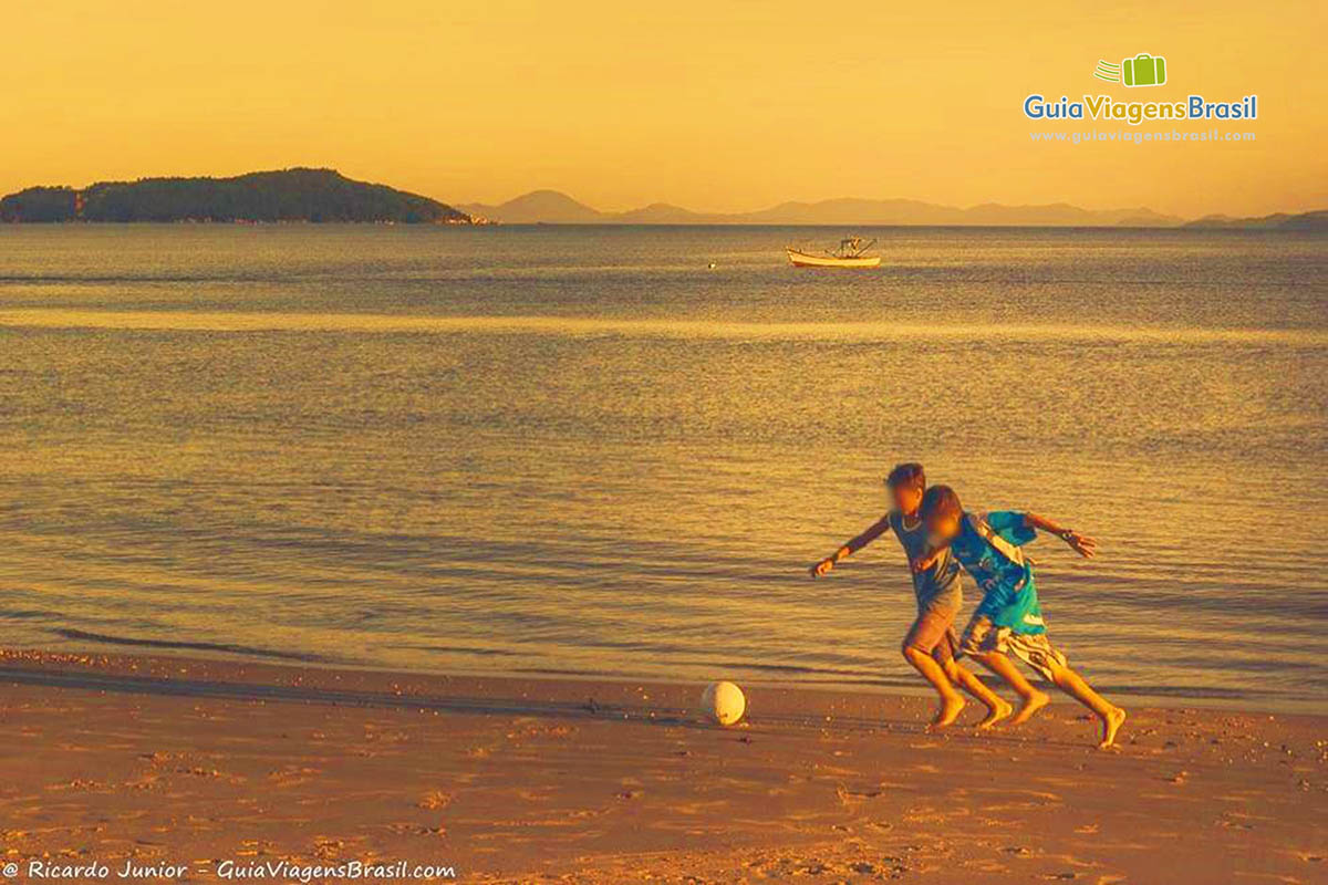 Imagem de crianças jogando bola na beira da praia.