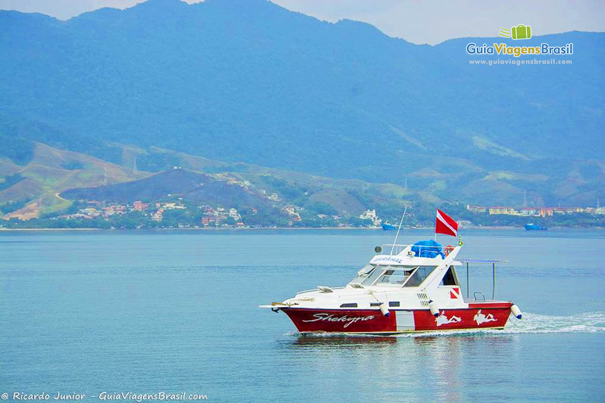 Imagem de uma lancha grande branca e vermelha no mar, em Ilhabela.