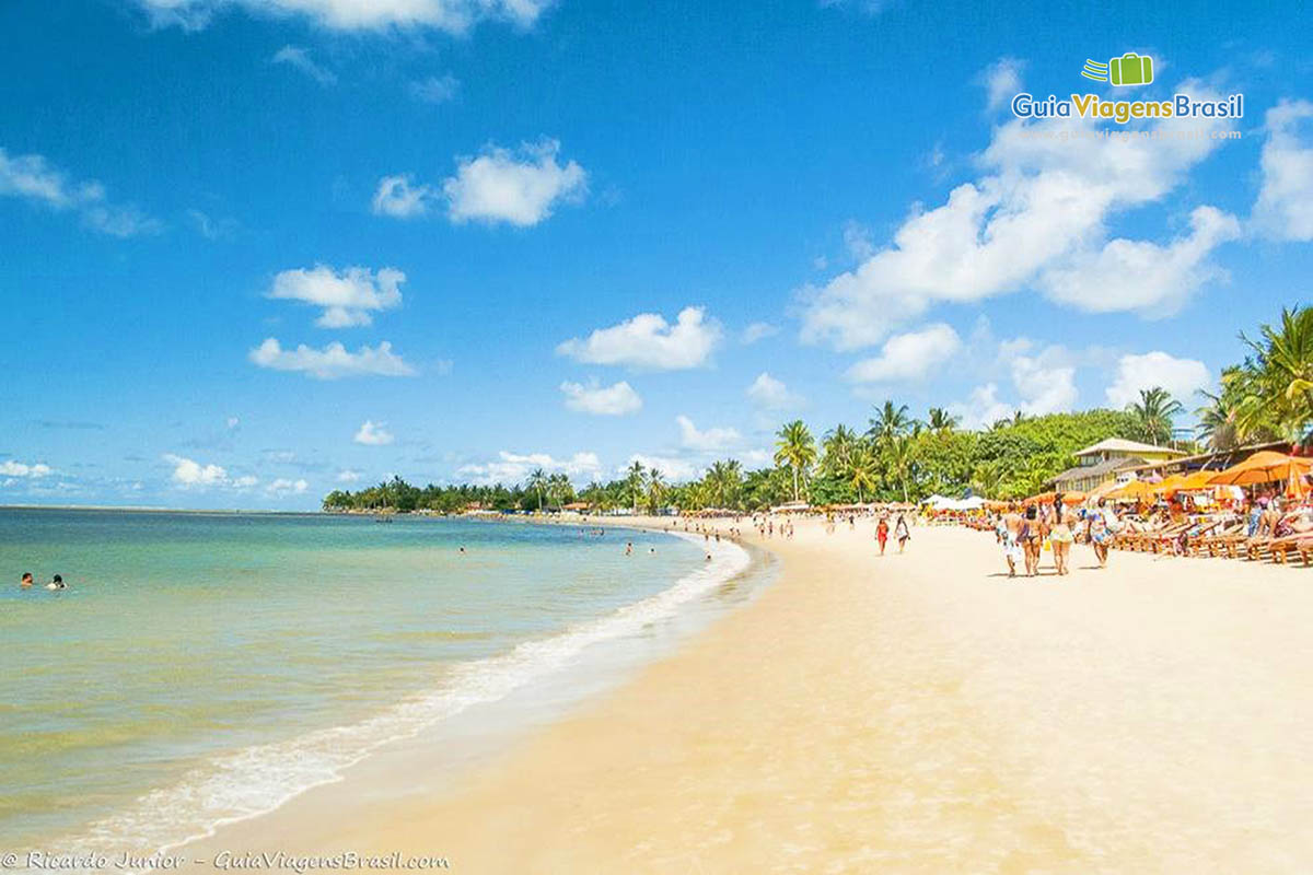 Imagem de turistas andando pelas areias da praia e ao fundo belos coqueiros.