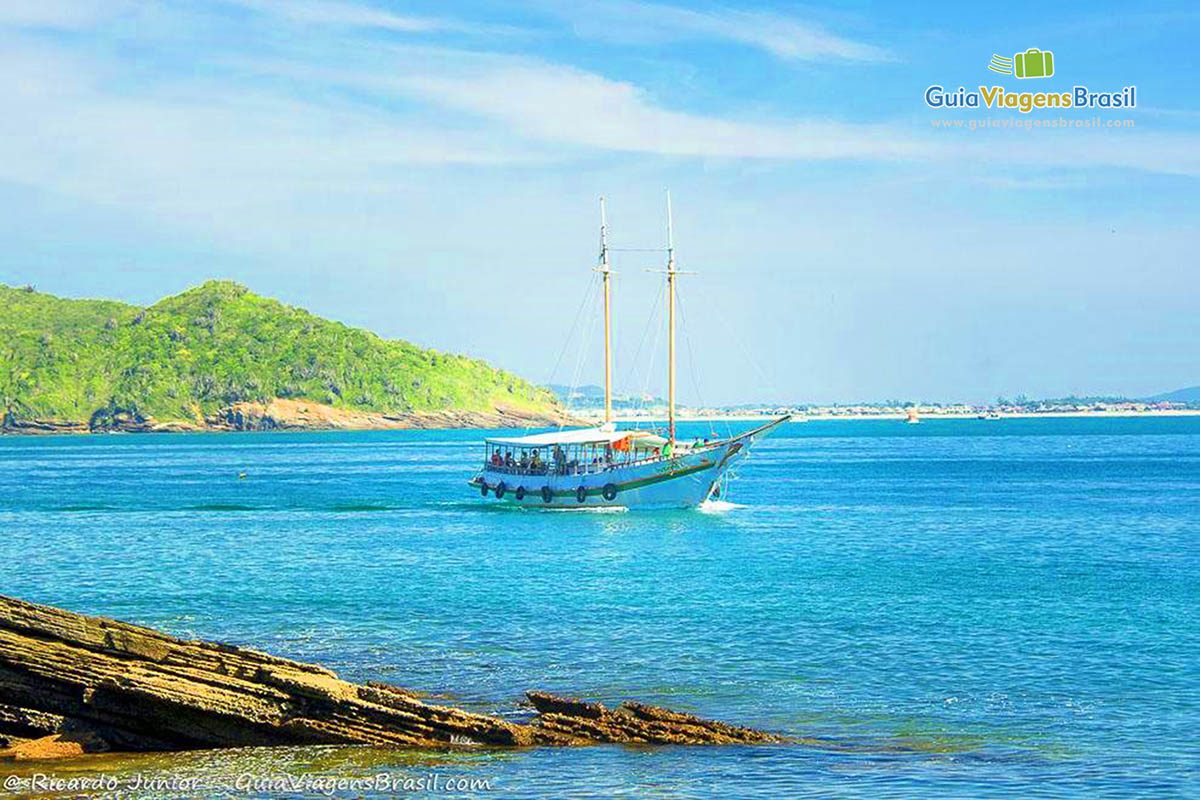 Imagem de uma pedra e ao fundo o um barco no mar fantástico, em Búzios.