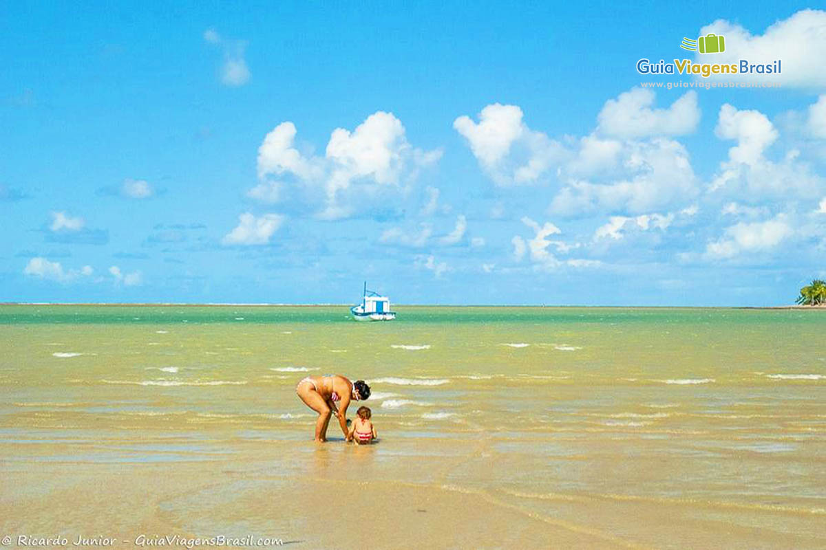 Imagem de mãe e filha se divertindo nas águas da praia.