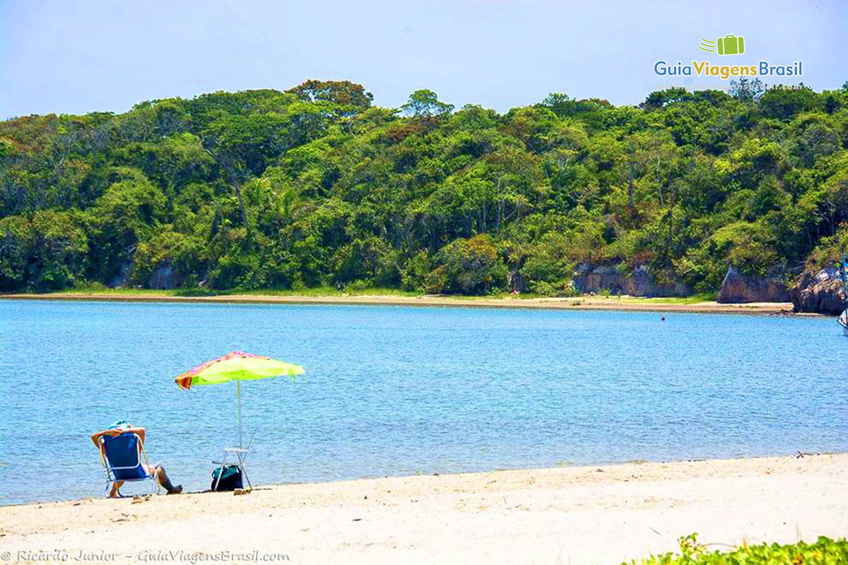 Imagem de uma pessoa sentado embaixo de guarda sol admirando o mar e a vegetação da Praia de Itaguaré.